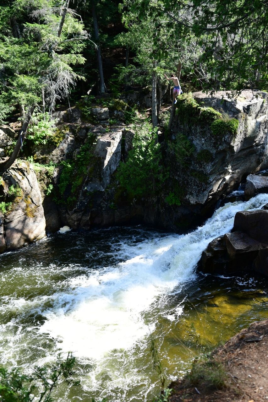 Cole standing at the top of a cliff above a waterfall swimming hole
